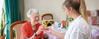 Ambulanter Pflegedienst eine junge Pflegerin überreicht einer Bewohnerin Medikamante